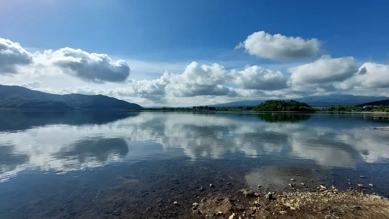 Paesaggio panoramico del lago con montagne sullo sfondo e nuvole nel cielo.