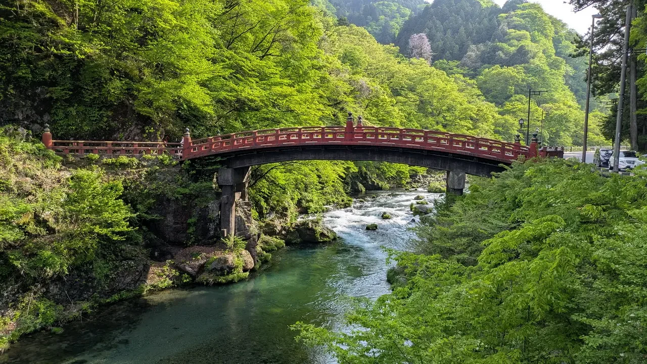 Ponte rosso su fiume verde in paesaggio montano giapponese.
