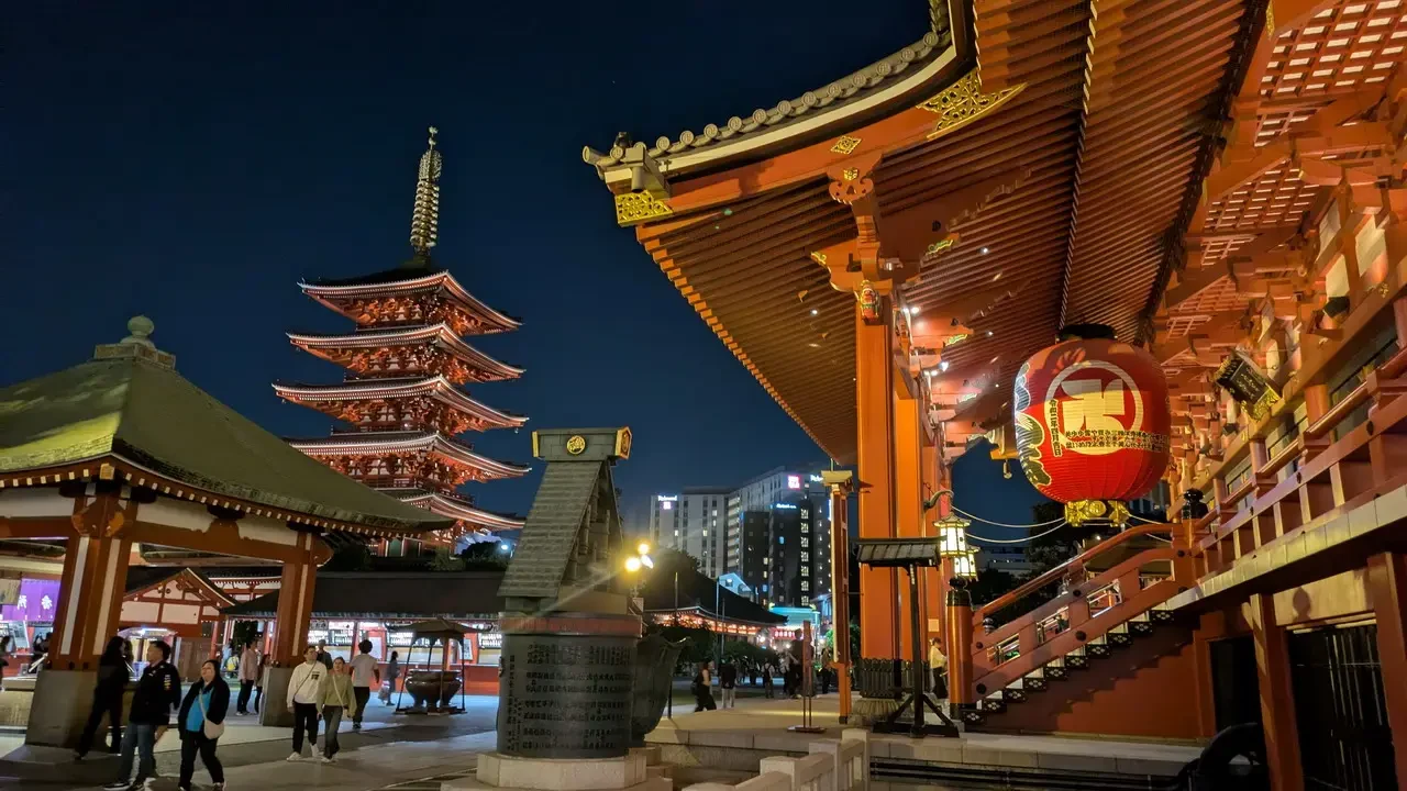 Vista notturna del Santuario Senso-ji a Tokyo con tetti tradizionali rossi e dorati.