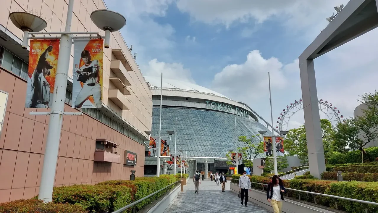Vista esterna del Tokyo Dome con edifici e persone in primo piano.