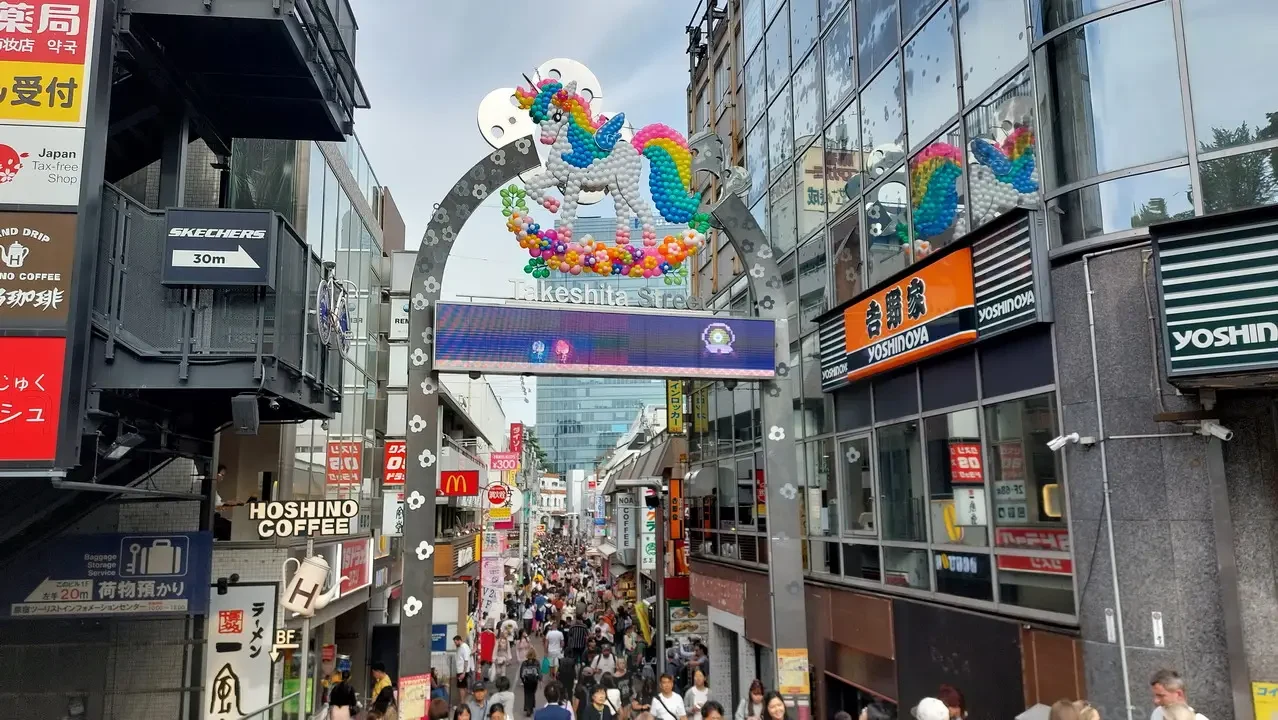 Una folla di persone cammina lungo una vivace strada commerciale a Tokyo con insegne colorate.