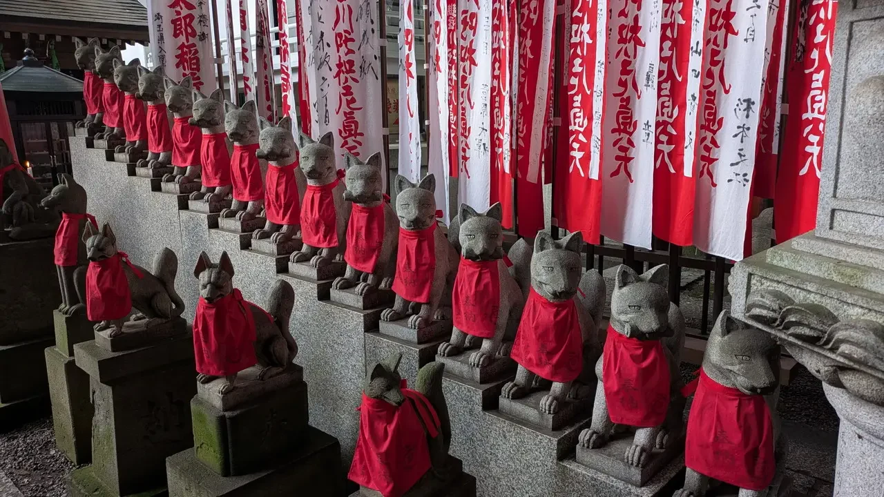 Statue di volpi vestite di rosso fiancheggiano una struttura del santuario.