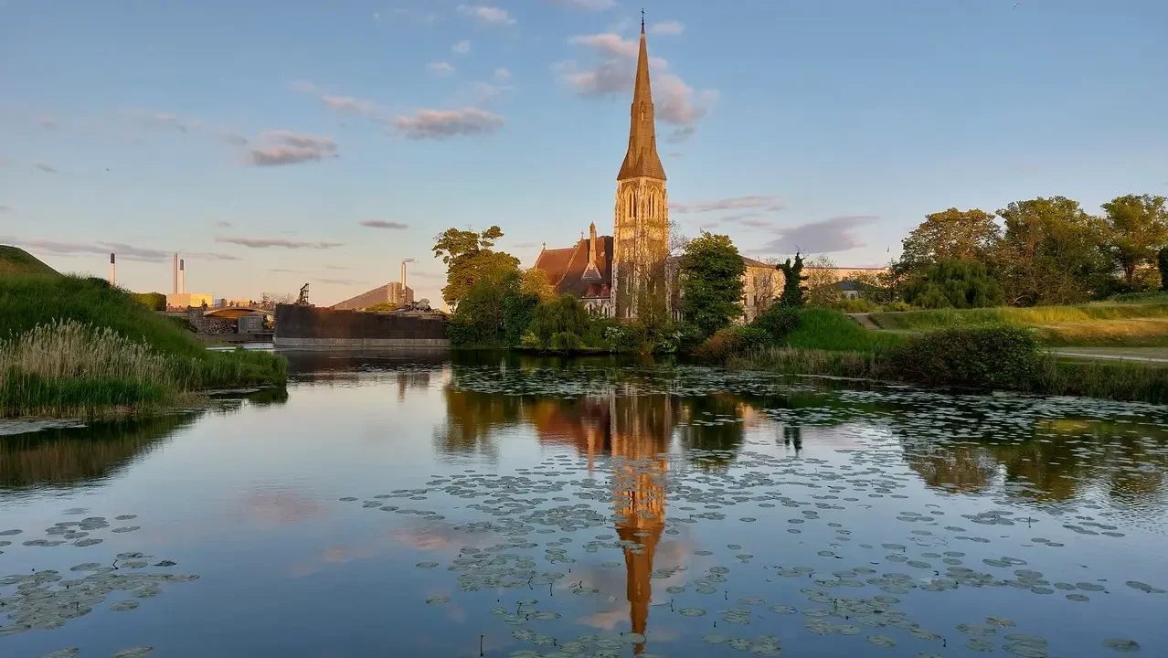 Riflesso della guglia di una chiesa sull'acqua calma al tramonto.
