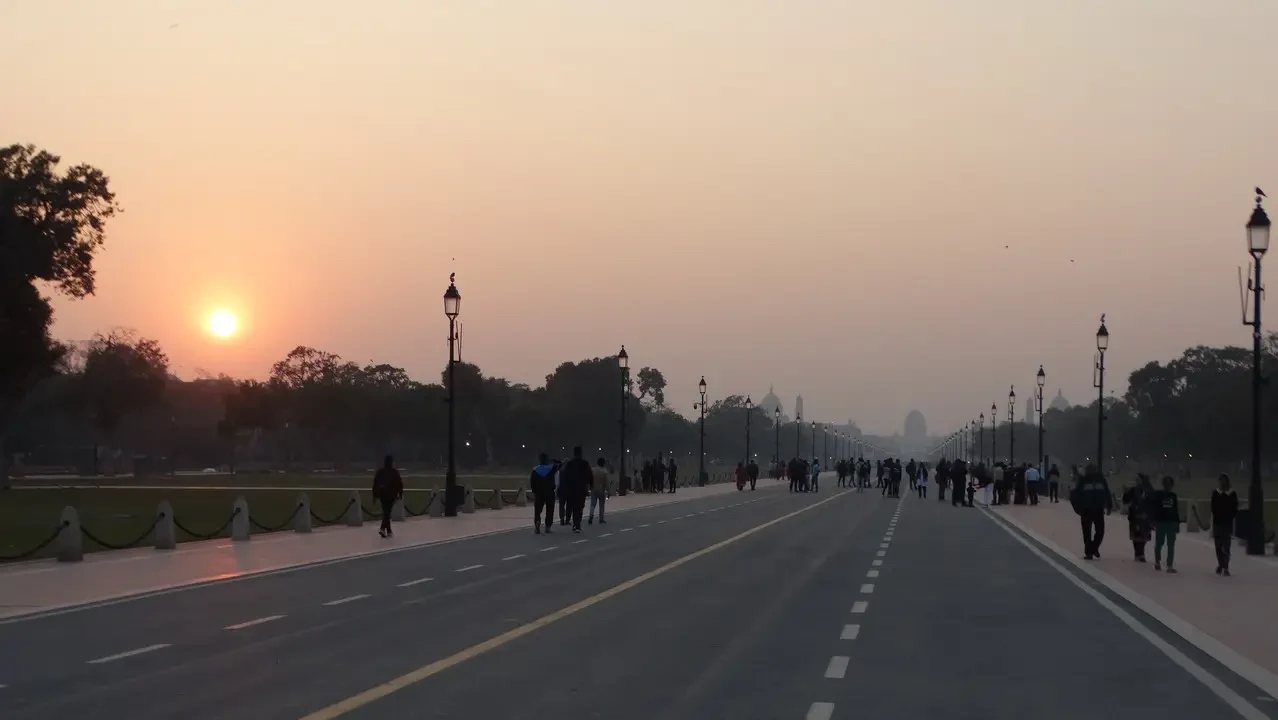 Un lungo viale con persone camminano al tramonto a Delhi, India.