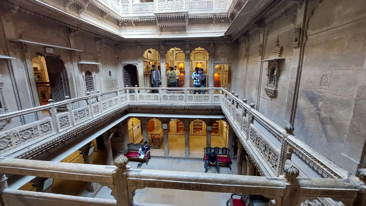 Interno sontuoso di un haveli indiano con balaustre decorata che mostra una vista su altre stanze.