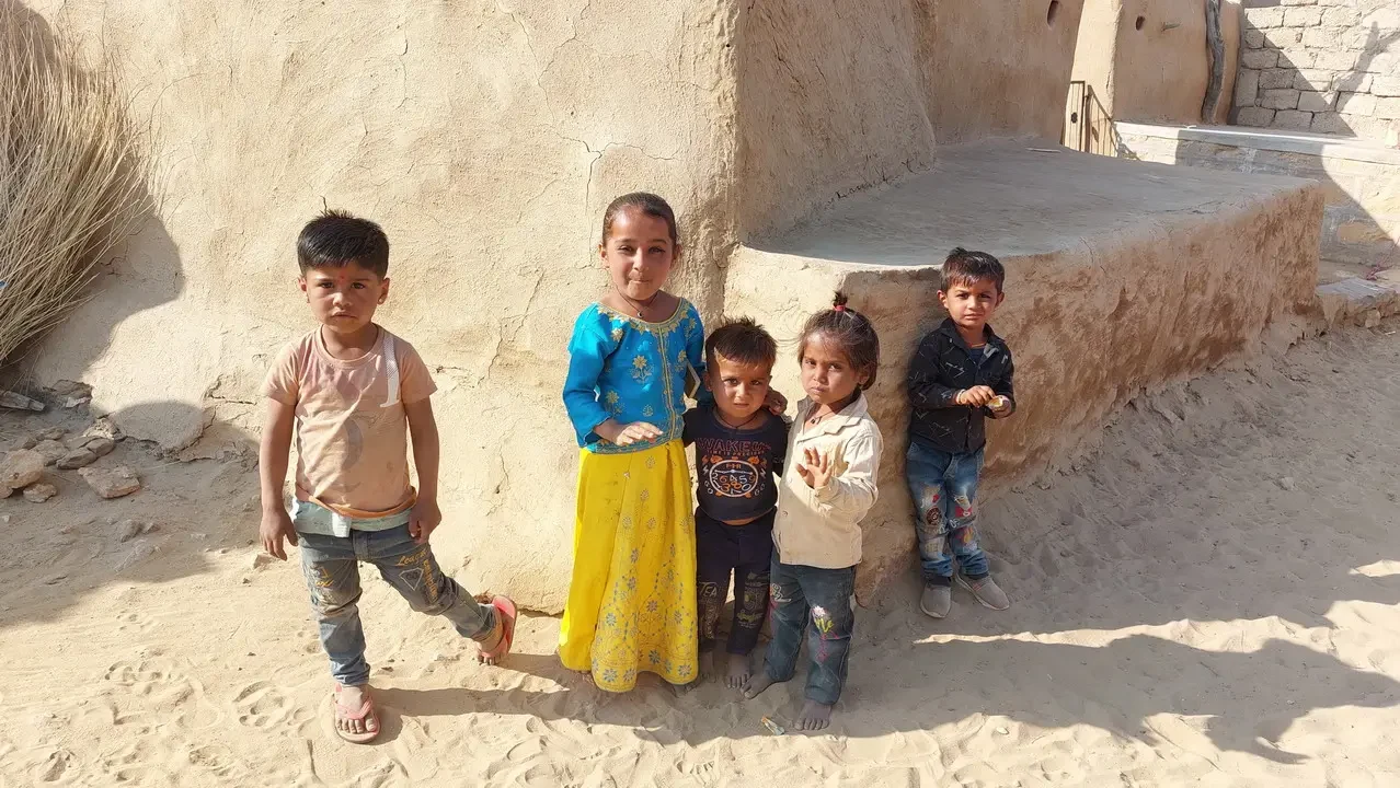 Bambini sorridono davanti a una struttura di fango nel deserto indiano.