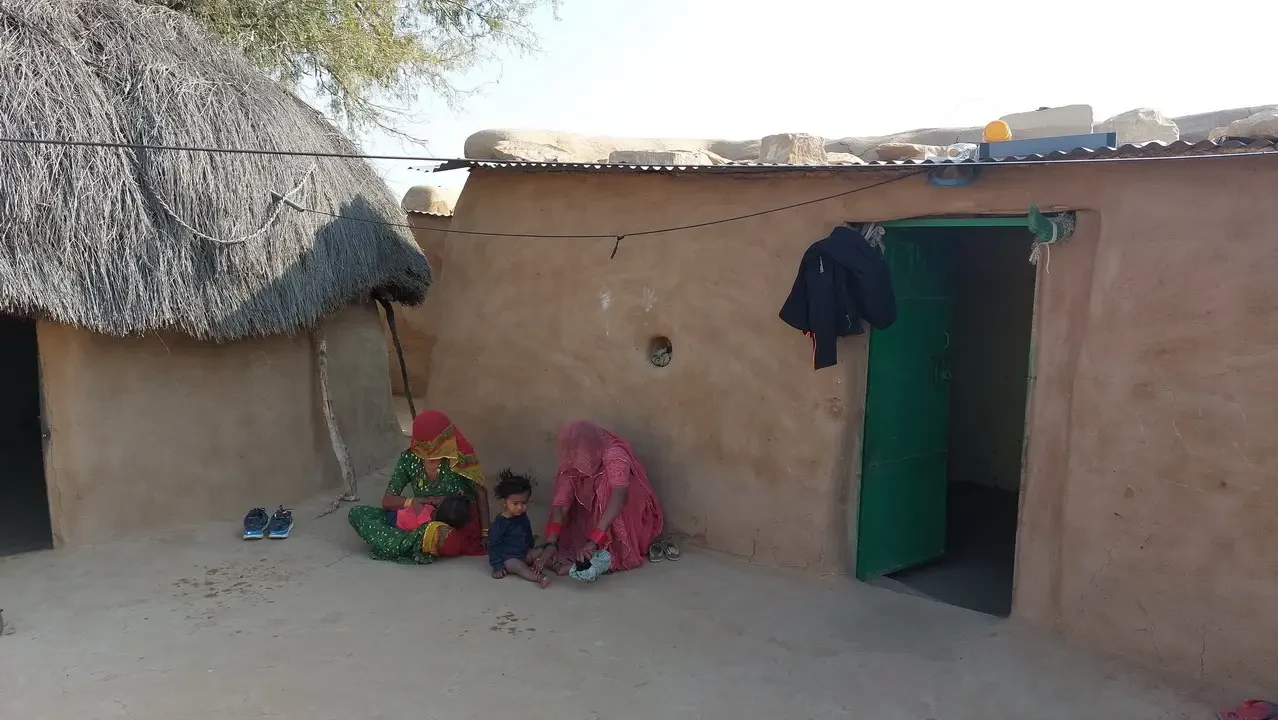 Una famiglia siede davanti a una casa in terra battuta nel deserto indiano.