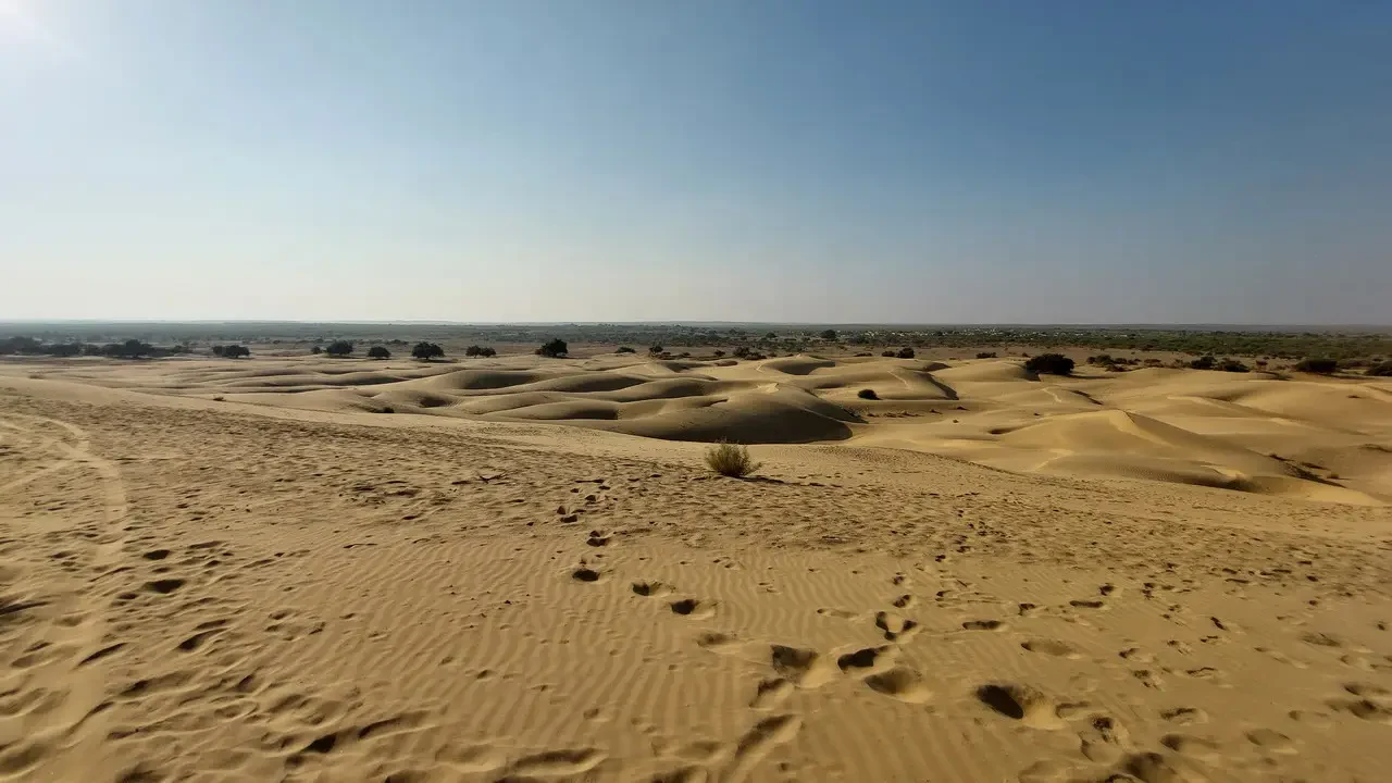 Vista ampia di dune del deserto sabbioso sotto un cielo azzurro.