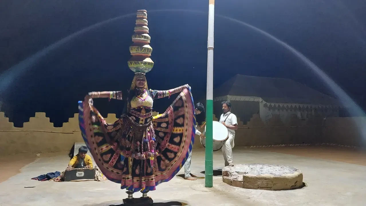 Un gruppo di persone e una scultura tradizionale sono presenti in un paesaggio desertico indiano.