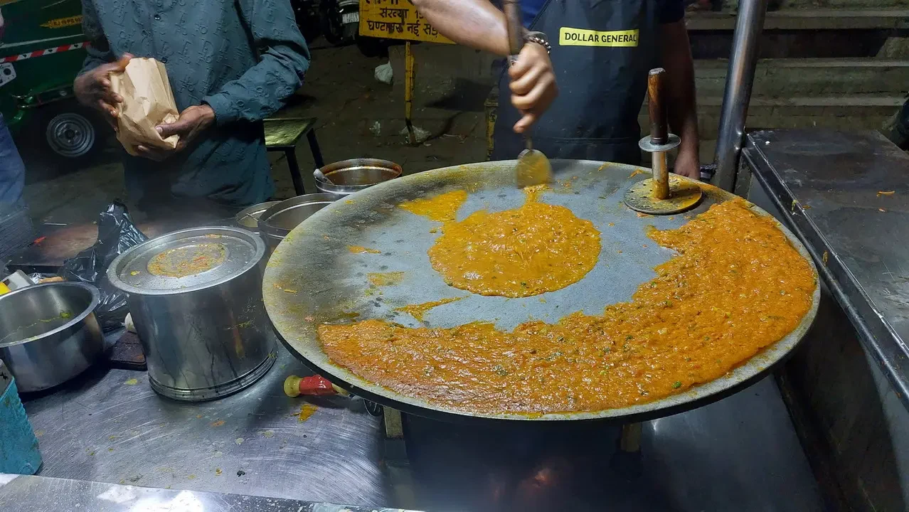 Un uomo prepara cibo in strada su una padella grande.