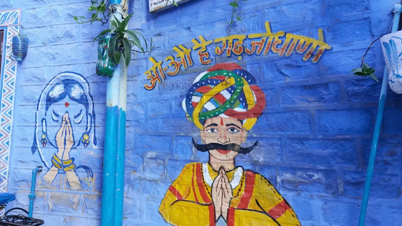 Murales tradizionali indiani su una parete blu mostrano figure con turbanti e espressioni serene.