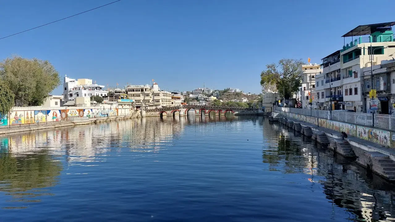 Vista di un canale tranquillo con edifici e un ponte in India.