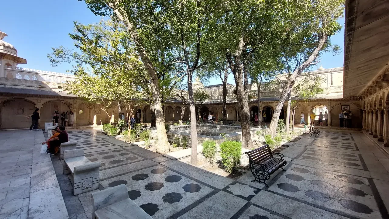 Cortile interno del palazzo di Udaipur con alberi e passeggiata ombreggiata.