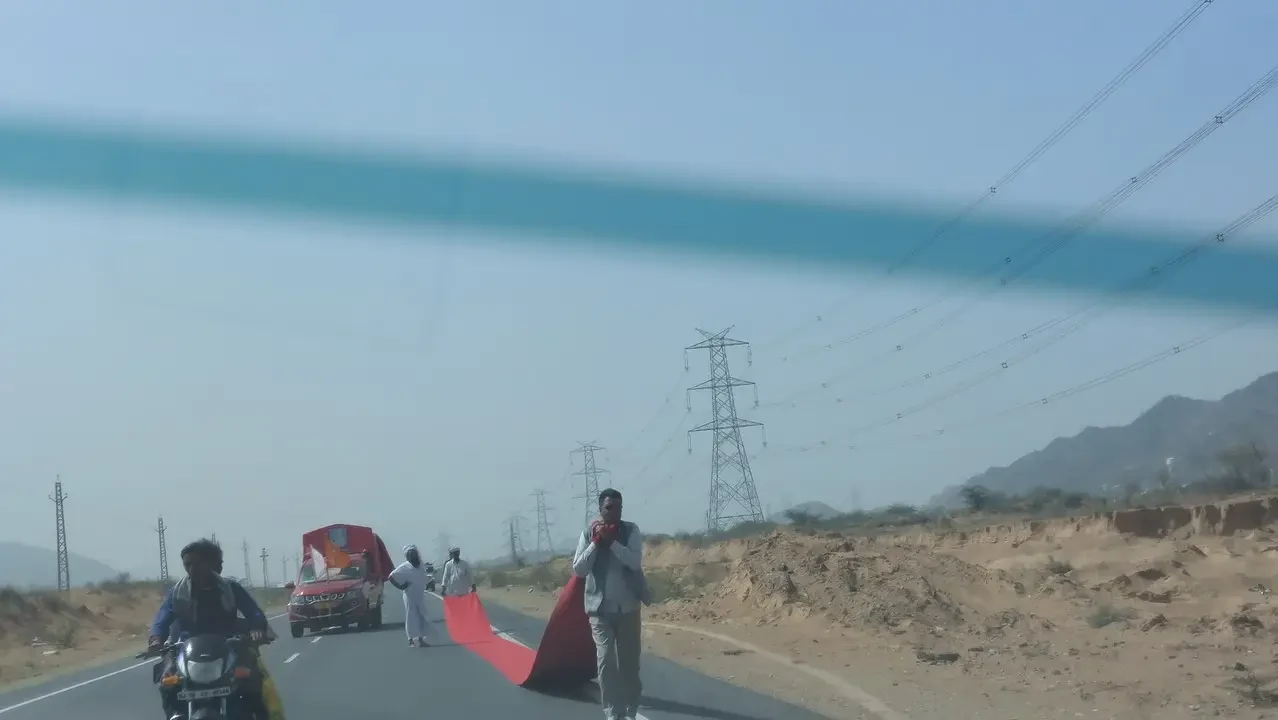 Una persona cammina su una strada di campagna in India con linee elettriche sopra di loro.
