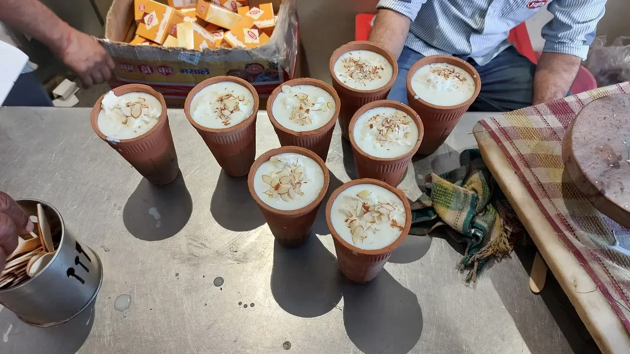 Una serie di bicchieri pieni di lassi con granella di pistacchio sono disposti su un tavolo all'aperto.
