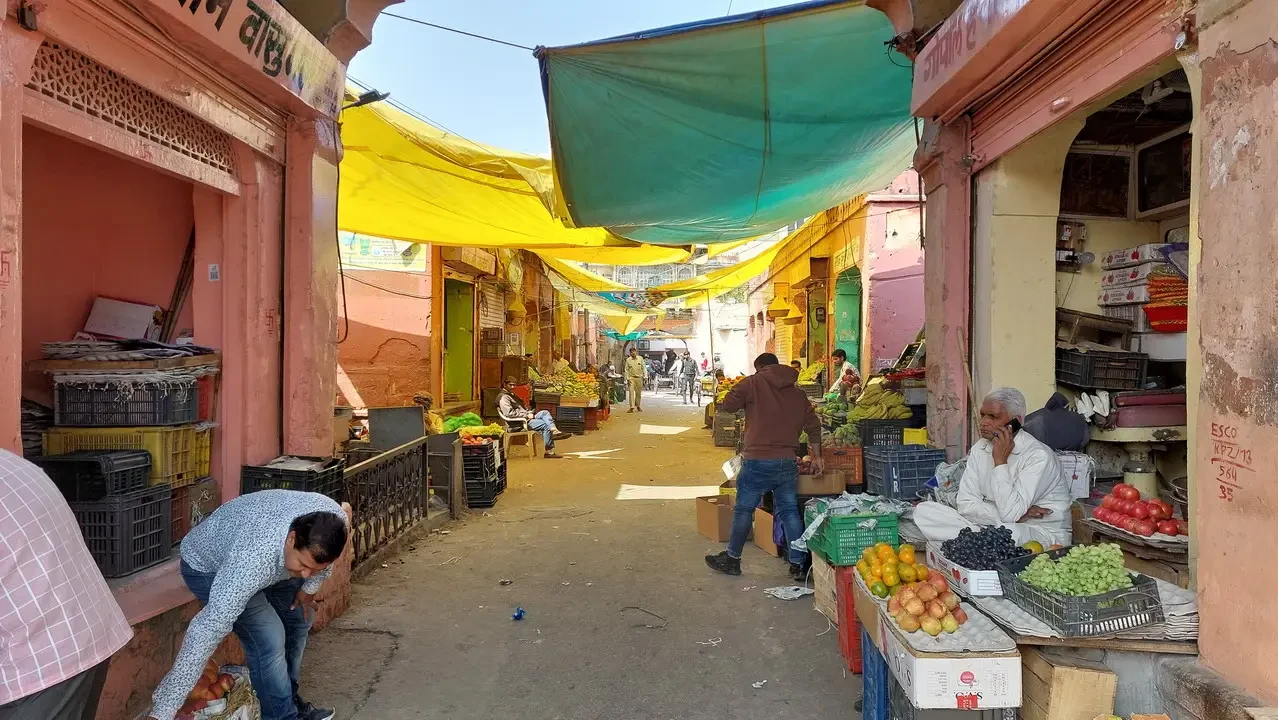 Una strada commerciale stretta in un mercato indiano pieno di bancarelle di frutta e verdura.