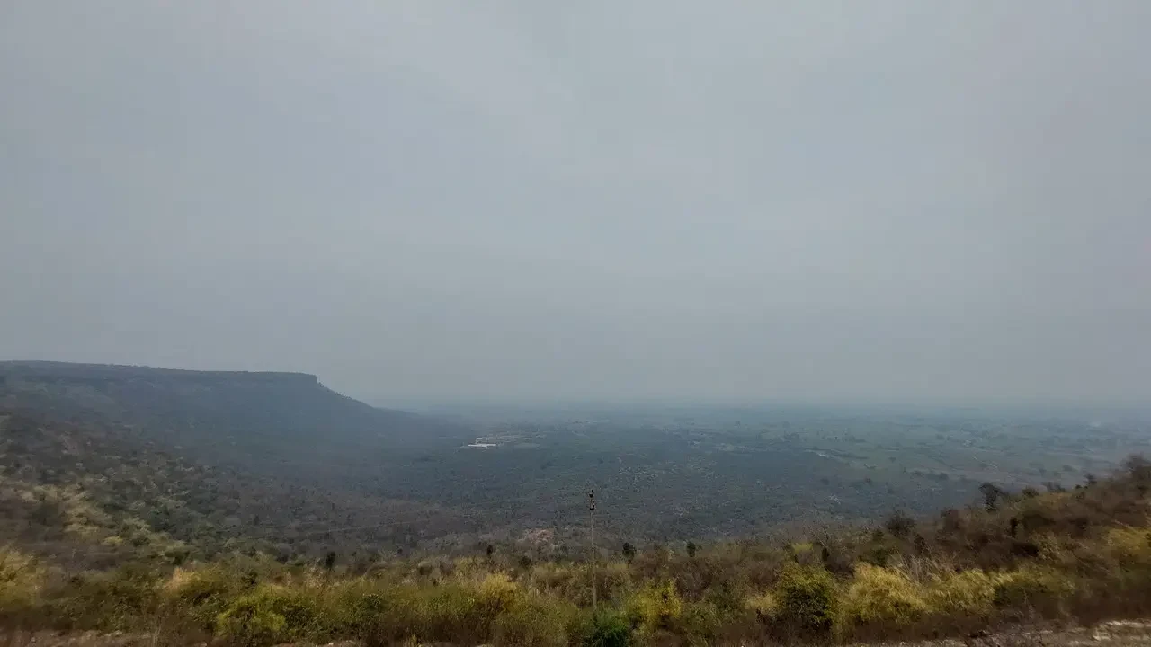 Paesaggio rurale e collinare in India con vegetazione secca sotto un cielo coperto.