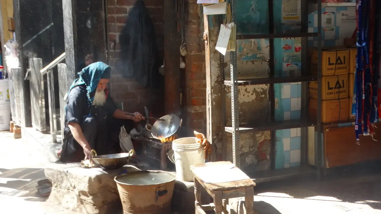 Un uomo cucina all'aperto usando pentole di metallo davanti a una facciata rustica.