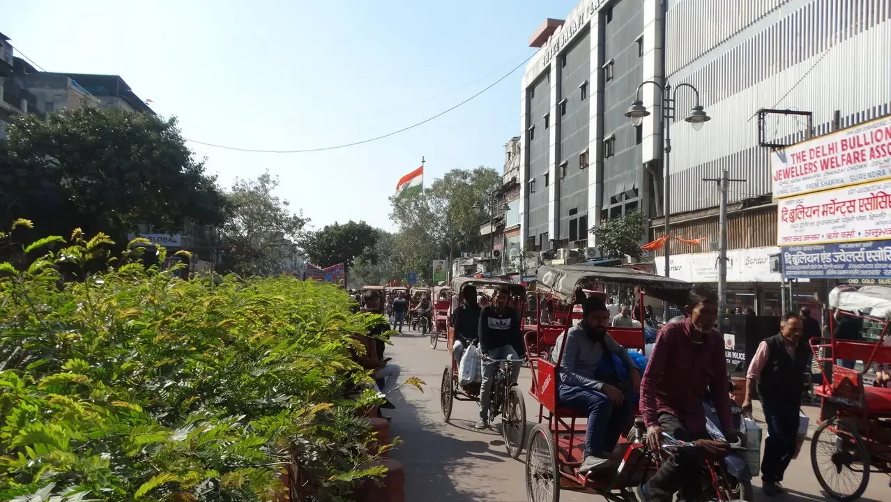 Una scena di strada a Delhi mostra veicoli in movimento tra gli edifici.
