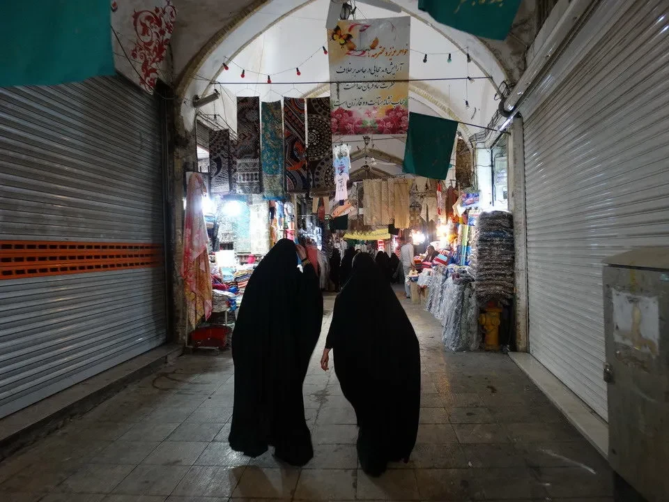Una vista interna di un mercato tradizionale in Iran con persone che passeggiano tra le bancarelle.