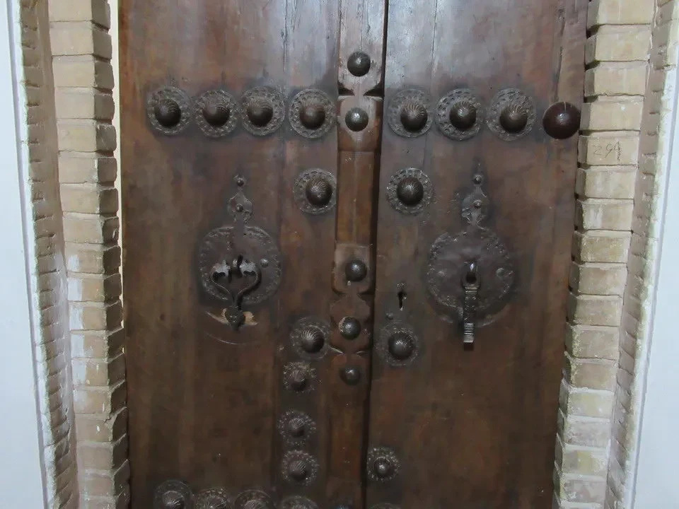 Porta di legno antica con decorazioni metalliche e rilievi.