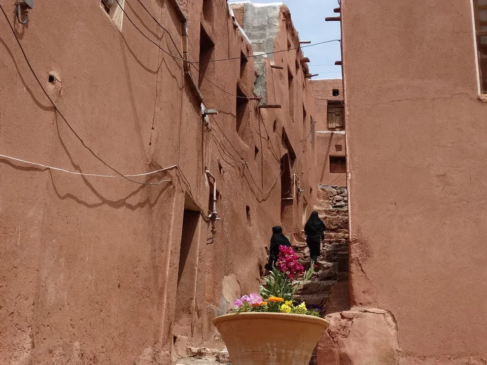 Una strada stretta e color ocra in un insediamento iraniano con case basse.