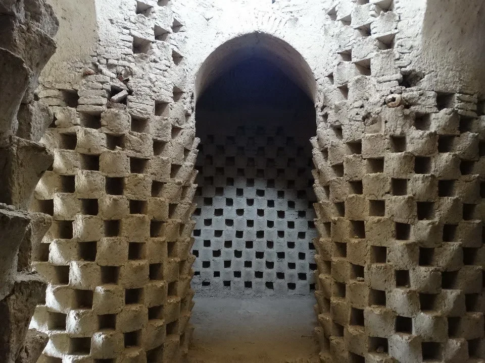 Una vista interna di un corridoio con pareti a blocchi in pietra irregolari e un arco in mattoni.