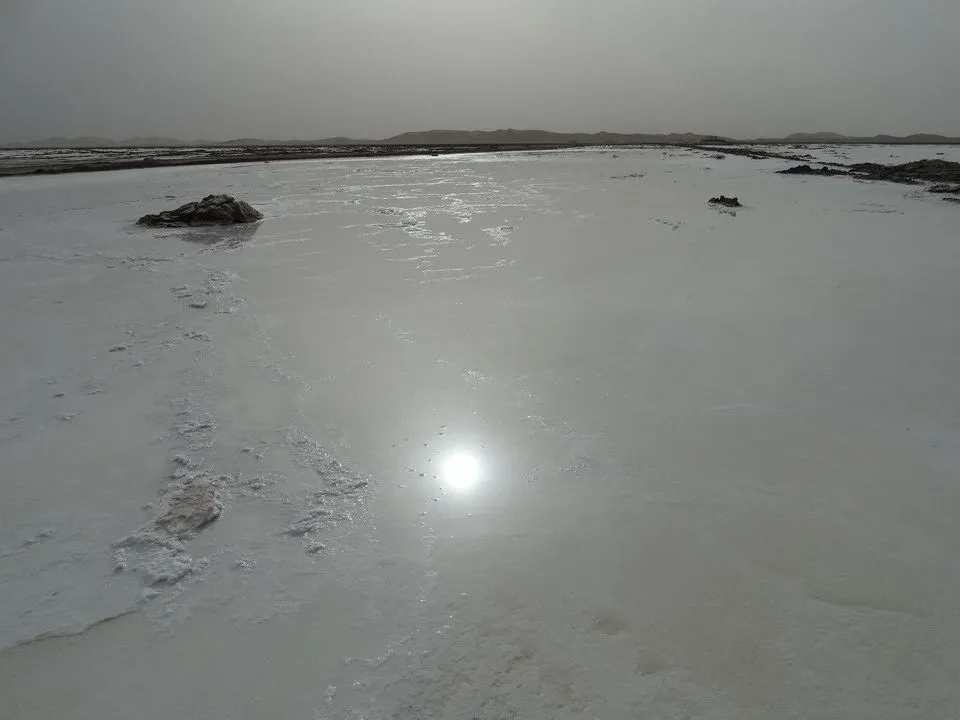 Un lago salato ghiacciato si estende sotto un cielo grigio.