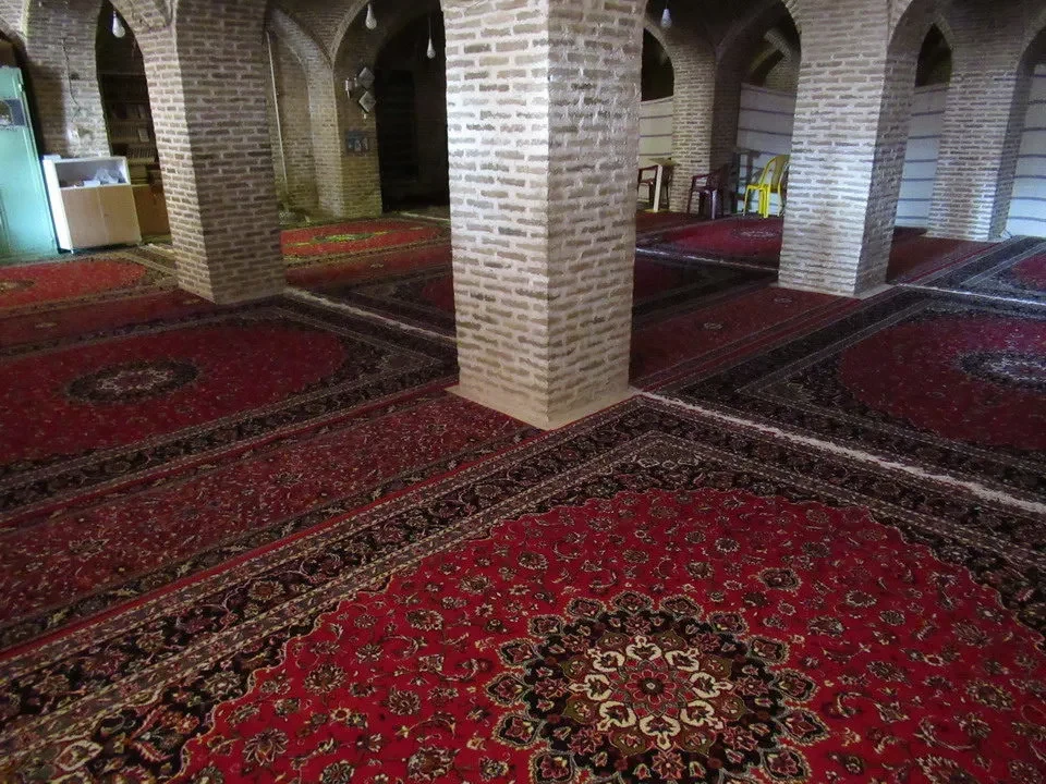 Interno di una moschea con pavimenti in tappeti rossi e archi in mattoni visibili.
