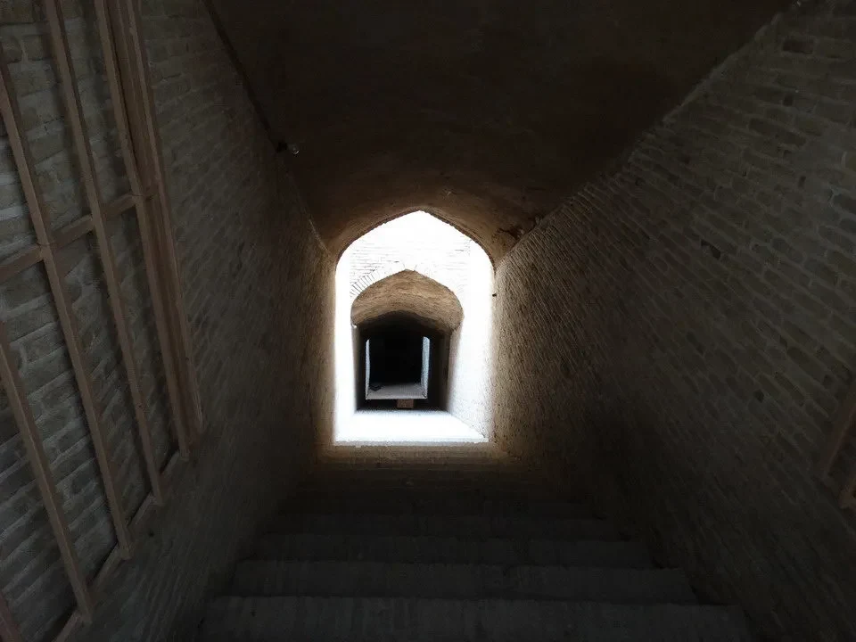 Corridoio interno con archi in mattoni che conduce a una luce brillante.