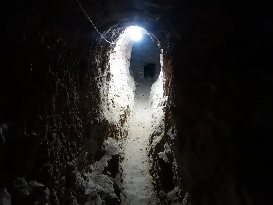 Passaggio stretto e scuro in una galleria sotterranea con luce alla fine.