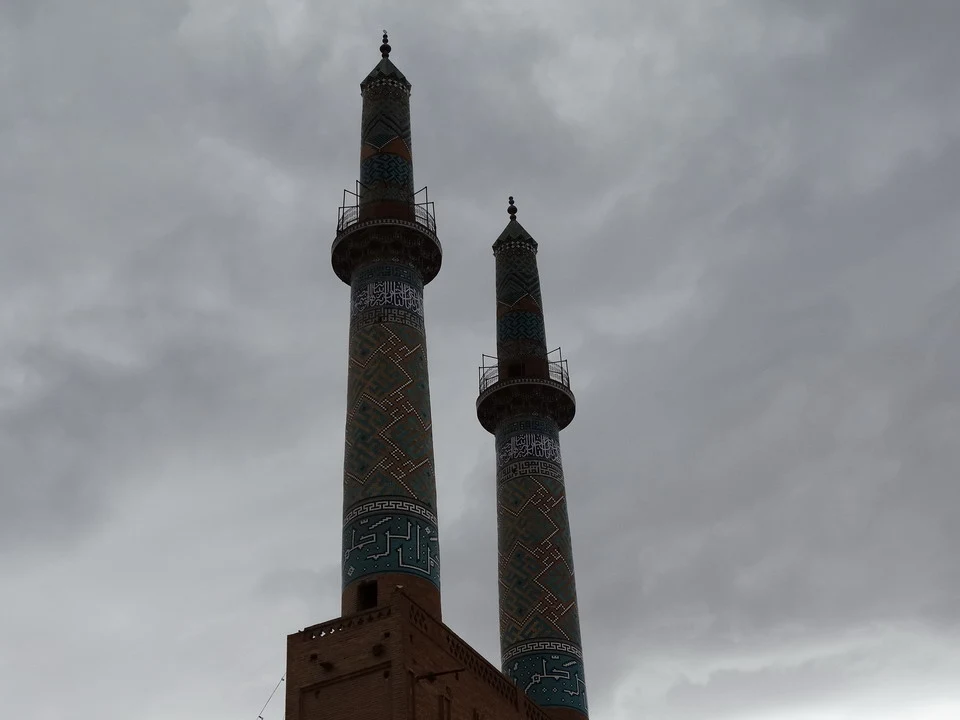 Due minareti in mattoni con decorazioni blu e turchesi dominano il cielo grigio.
