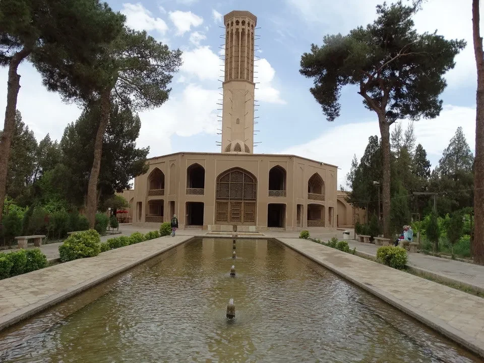 Cortile interno di un complesso architettonico iraniano con una torre centrale e un bacino d'acqua in primo piano.