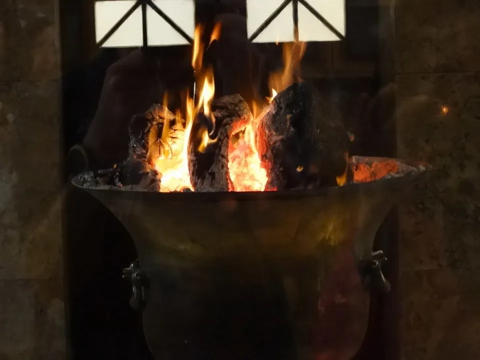 Fuochi ardenti bruciano in una grande pentola in un ambiente interno.