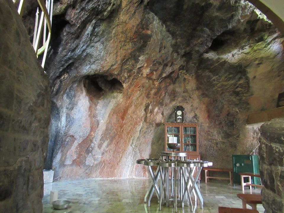 Interno di una grotta rocciosa con pareti ricoperte di rocce rosse e strutture interne.