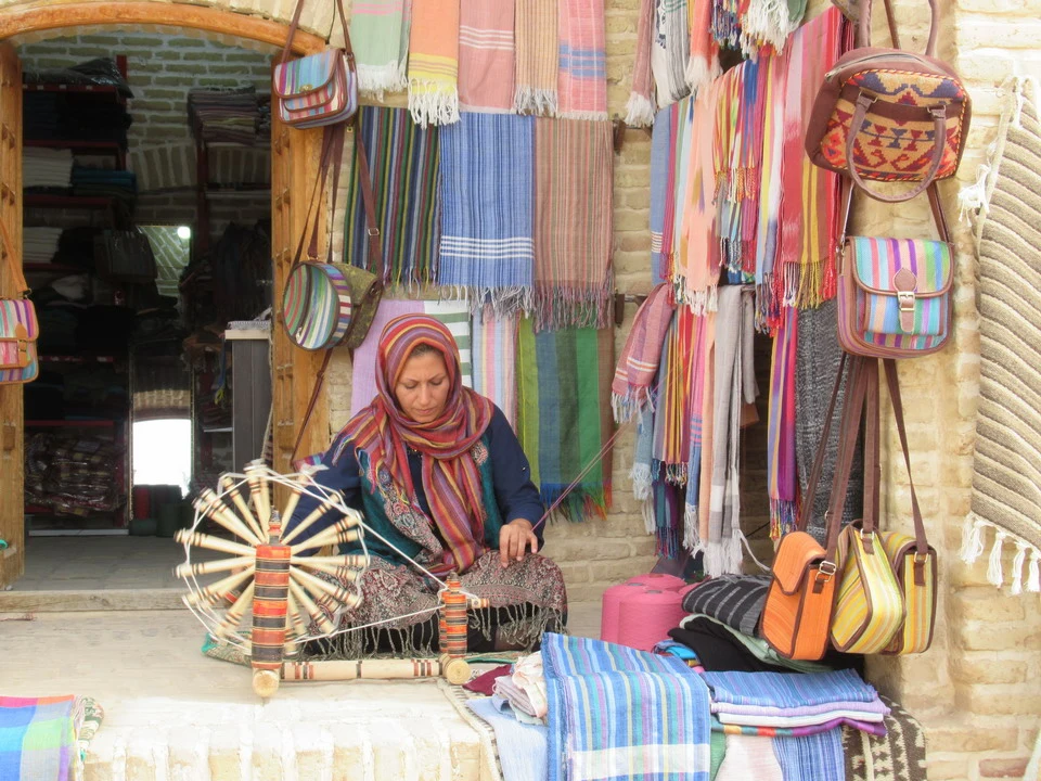 Una donna è seduta davanti a un negozio pieno di tessuti colorati in un caravanserraglio iraniano.