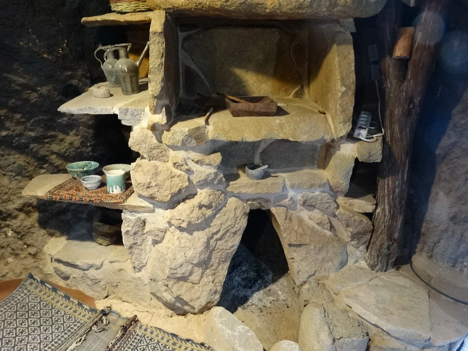 Interno di una grotta con una stanza rustica e antiche strutture in pietra.