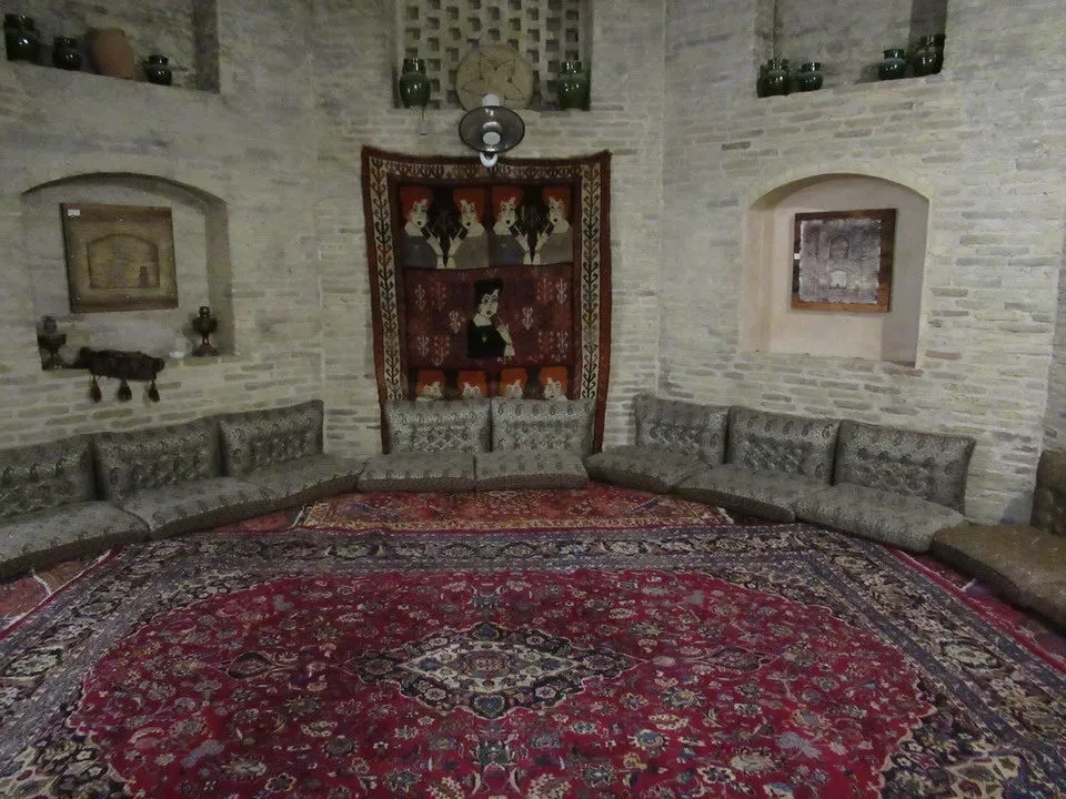 Interno storico decorato con pareti in pietra e tappeti riccamente drappeggiati.