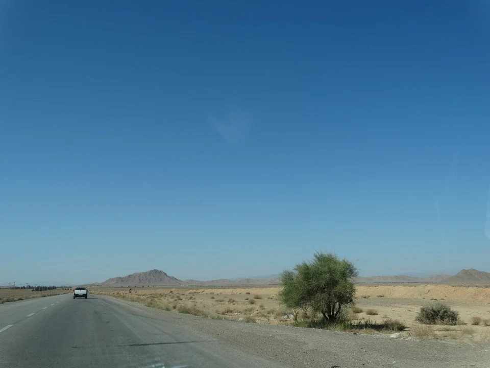 Una strada asfaltata attraversa un paesaggio arido in Iran sotto un cielo azzurro.
