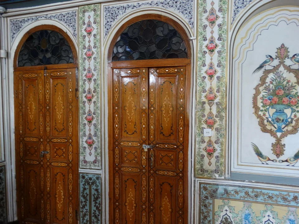 Porte in legno decorate con pannelli e fregi colorati in un interno tradizionale iraniano.