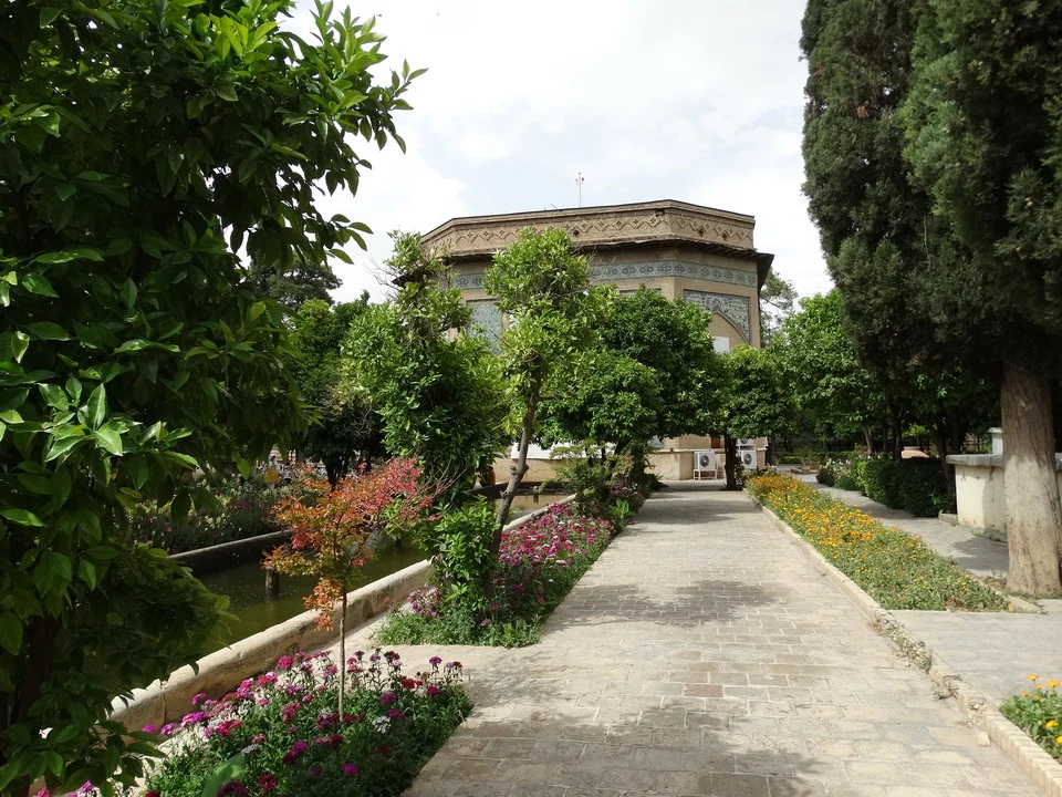 Un viale alberato con un edificio tradizionale in stile persiano e un corso d'acqua in primo piano.