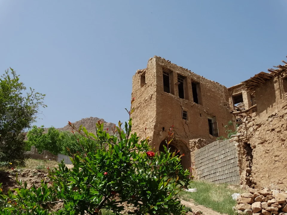 Una vecchia struttura in terra cotta con un cortile e vegetazione circostante in Iran.
