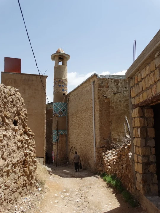 Una strada sterrata passa tra edifici in pietra in Iran.
