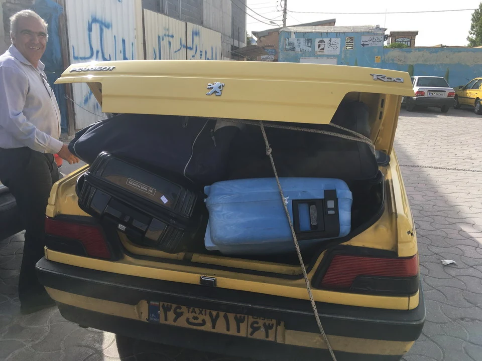 Un uomo sorride davanti al bagagliaio di un taxi giallo in Iran.