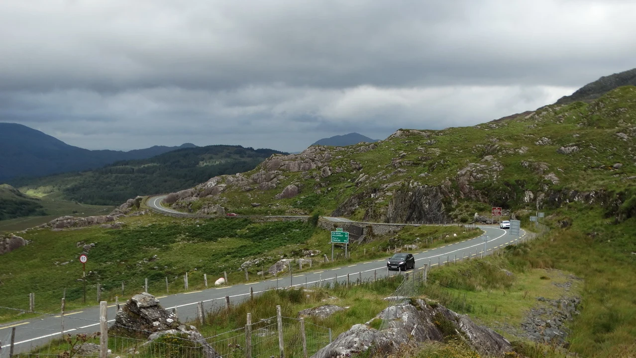 Una strada sinuosa attraversa un paesaggio collinare in Irlanda sotto un cielo nuvoloso.