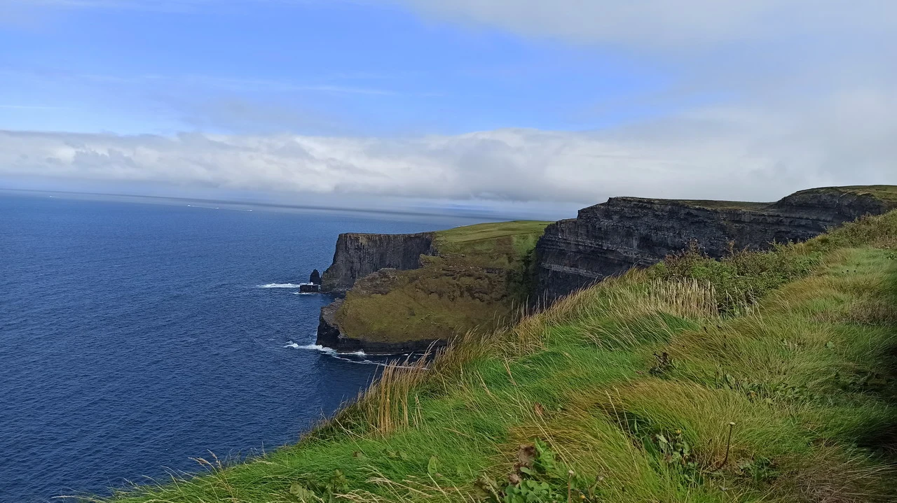 Le imponenti scogliere della costa di Moher in Irlanda si tuffano nel mare blu sotto un cielo nuvoloso.