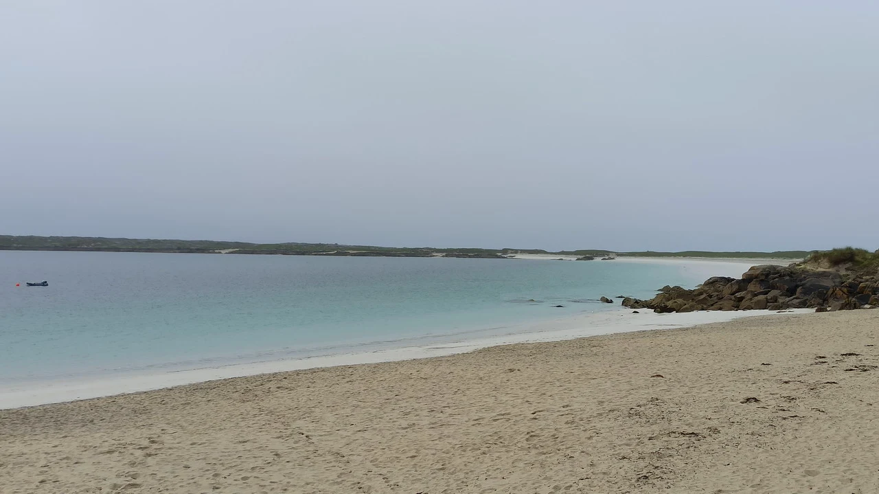 Una spiaggia sabbiosa si estende verso l'orizzonte con acqua turchese calma.