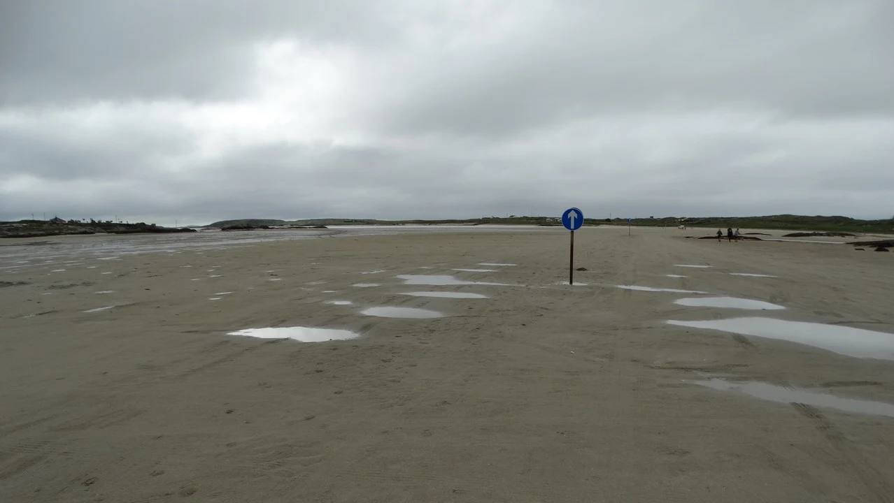 A vast expanse of wet sand stretches under a cloudy sky in Ireland.