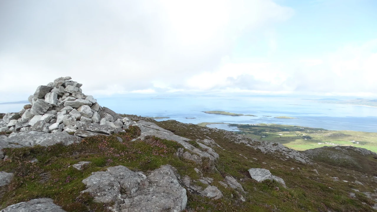 Paesaggio montano e costiero in Irlanda con rocce e vegetazione bassa sotto un cielo nuvoloso.