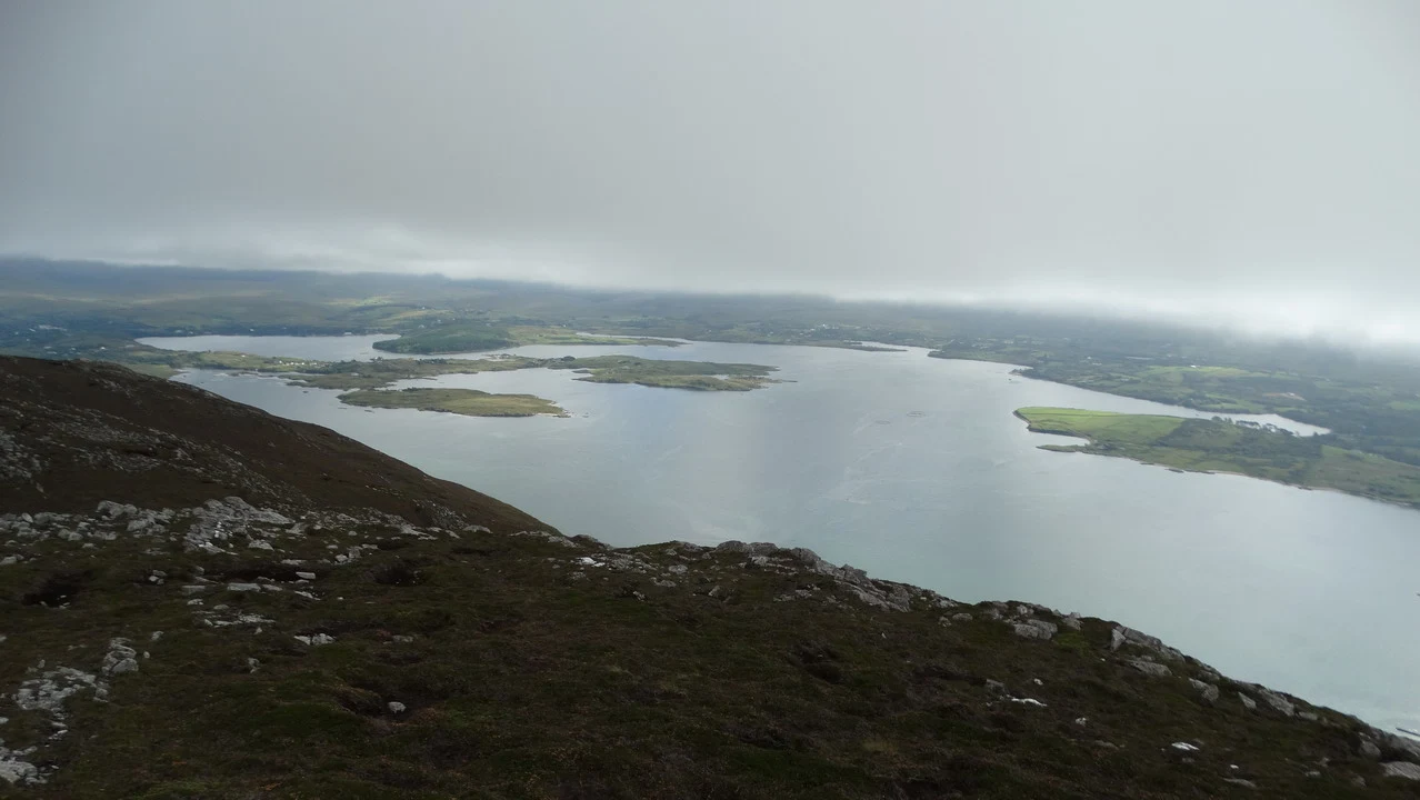 Paesaggio irlandese nebbioso con corpi d'acqua e colline ondulate.